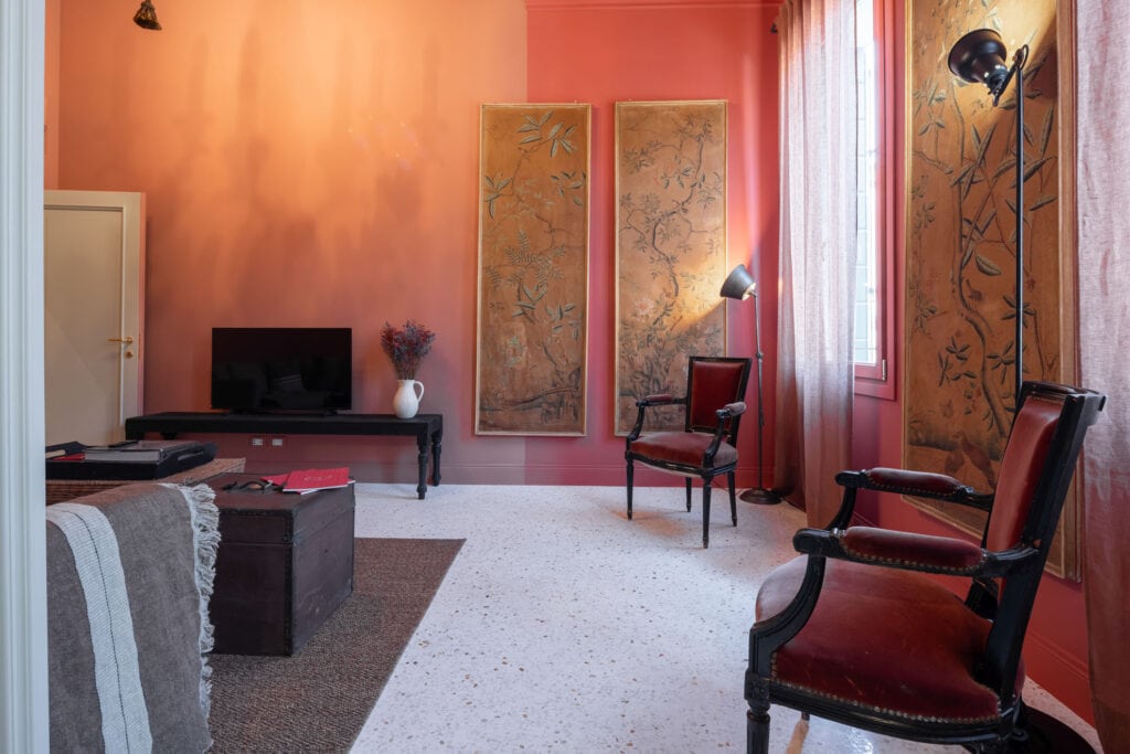 Warm and stylish living room with colorful walls, large sofa and bright windows overlooking the canal, in the Ca’ Maddalena – Sole apartment